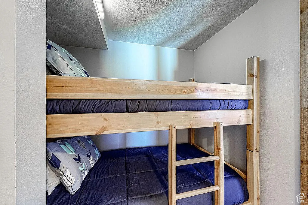 Unfurnished bedroom featuring a textured wall, a textured ceiling, and lofted ceiling