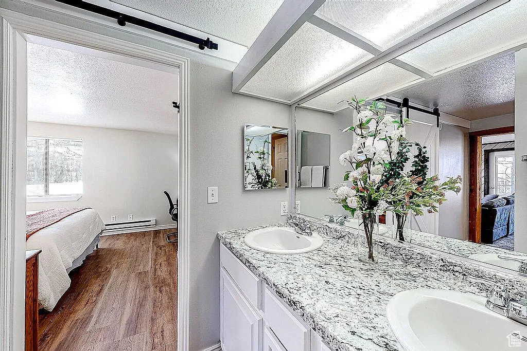 Ensuite bathroom with a baseboard radiator, wood finished floors, a sink, a textured ceiling, and connected bathroom