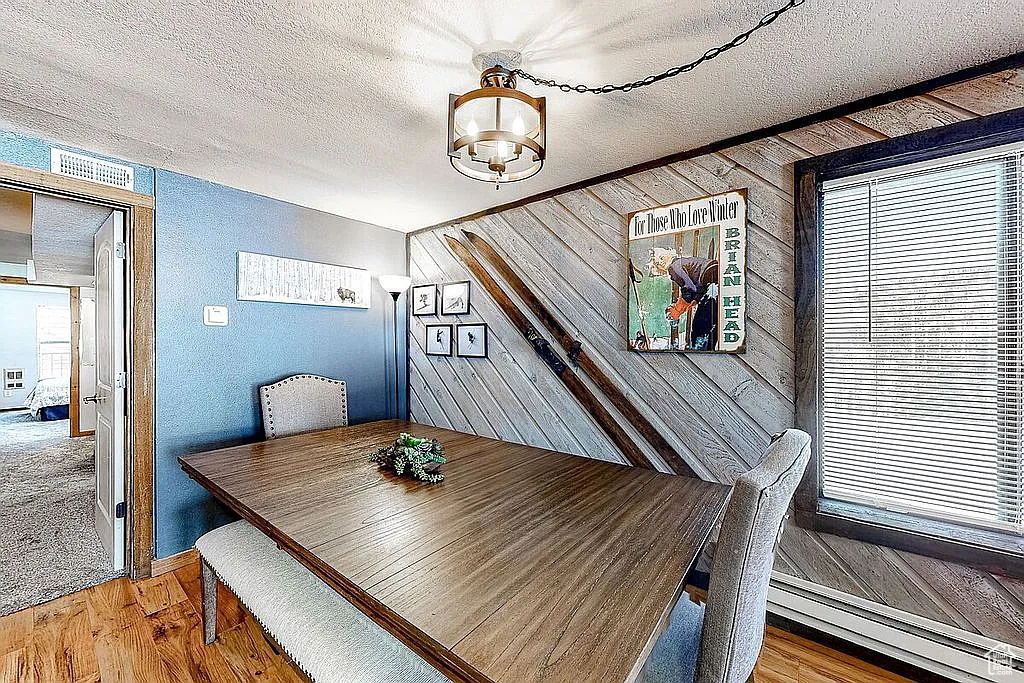 Dining area with a wealth of natural light, a textured ceiling, a notable chandelier, wood finished floors, and wooden walls