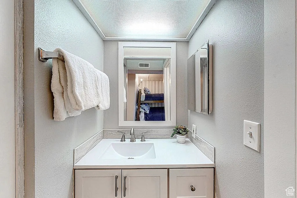 Bathroom with a textured wall, vanity, and visible vents