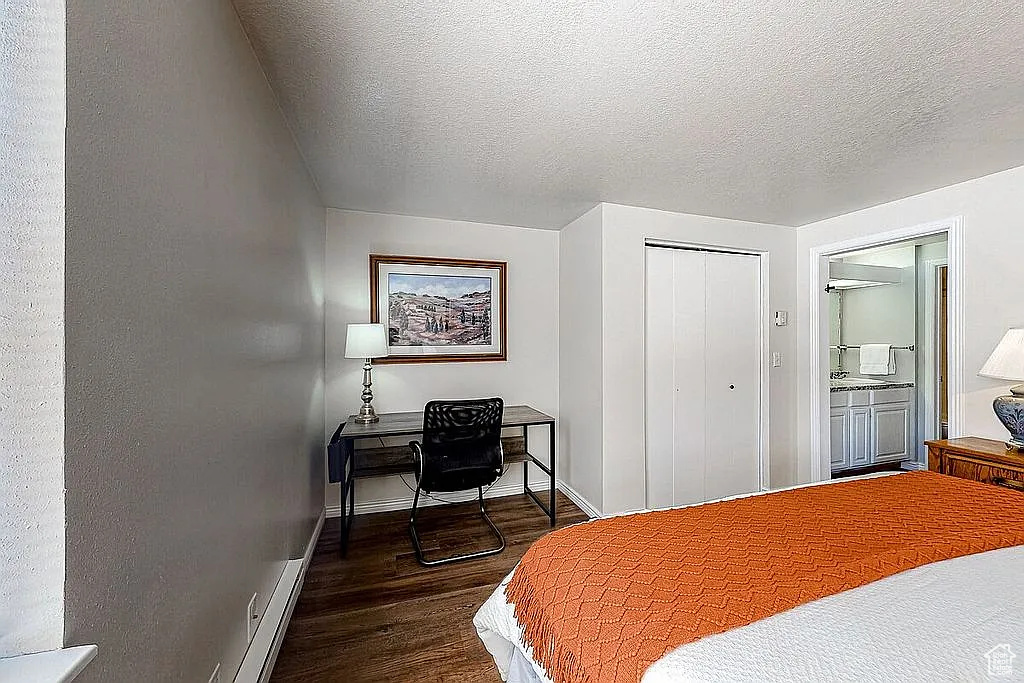 Bedroom featuring a textured ceiling, wood finished floors, ensuite bathroom, a closet, and baseboards
