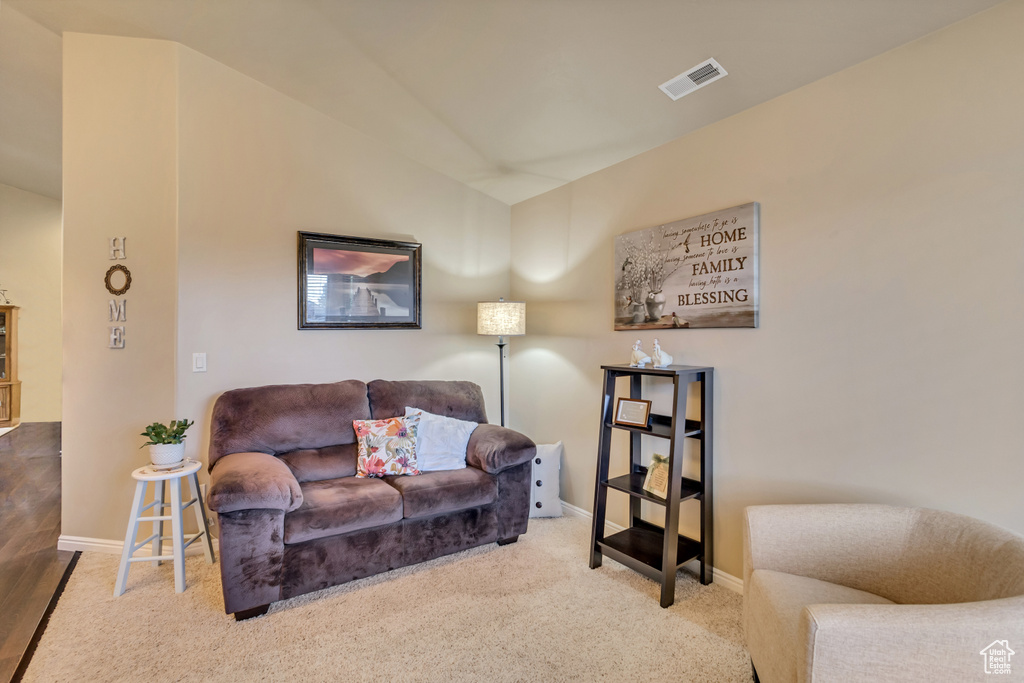 Carpeted living room with baseboards, vaulted ceiling, and visible vents