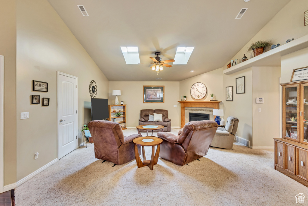 Living room with carpet flooring, visible vents, vaulted ceiling with skylight, and a fireplace