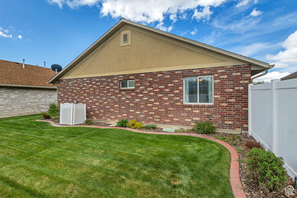 View of side of property with a yard, brick siding, and fence