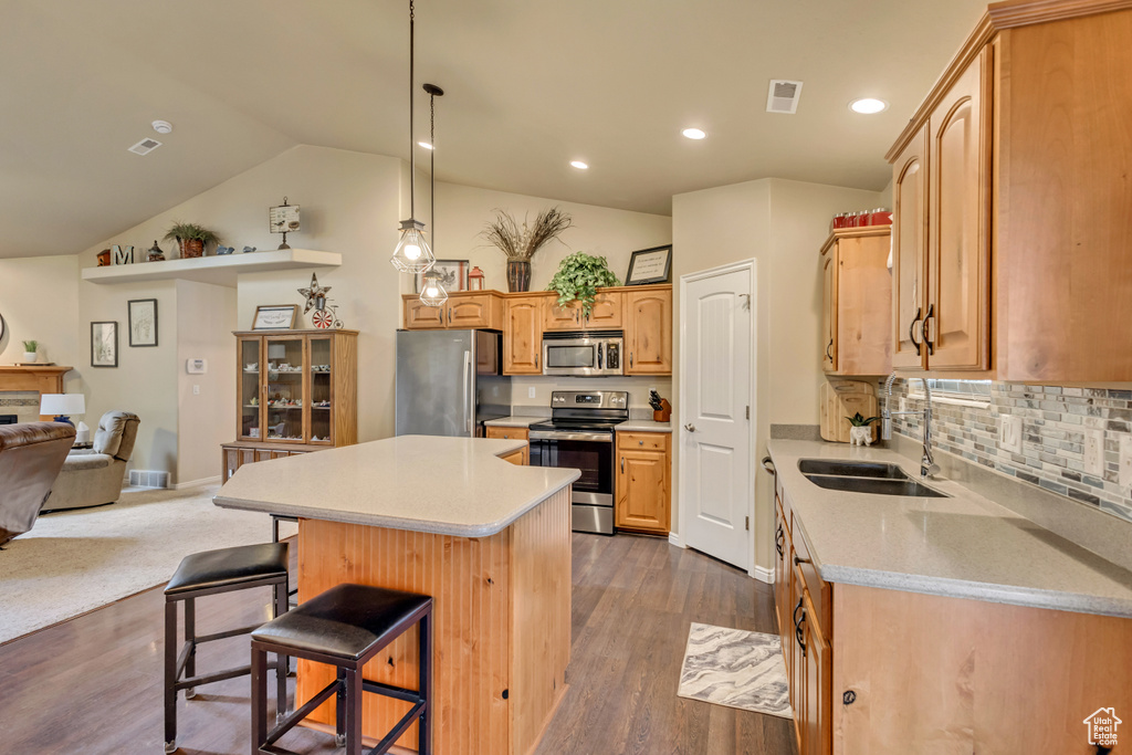 Kitchen featuring a breakfast bar area, appliances with stainless steel finishes, a center island, a sink, and light countertops