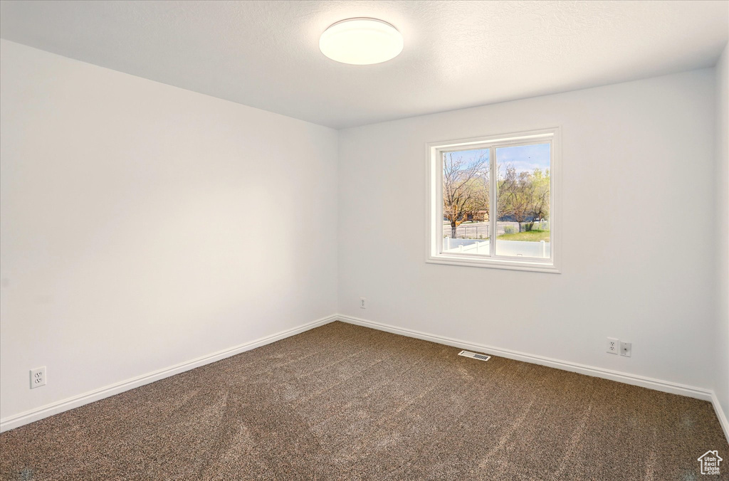 Spare room featuring dark carpet, baseboards, and visible vents