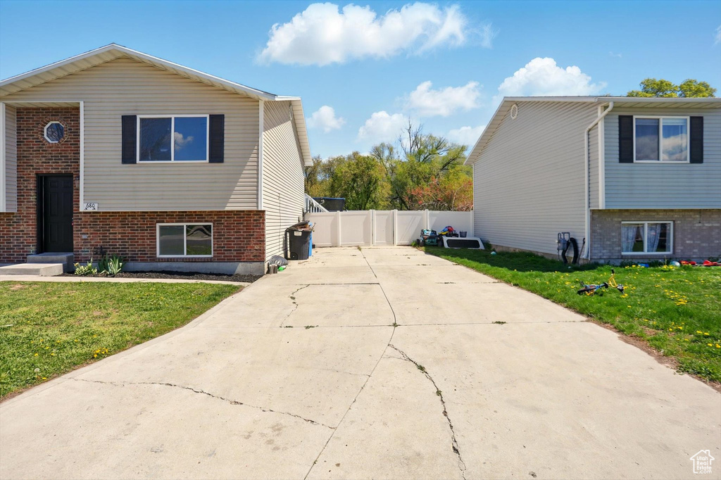 View of side of property featuring brick siding, a lawn, fence, and concrete driveway