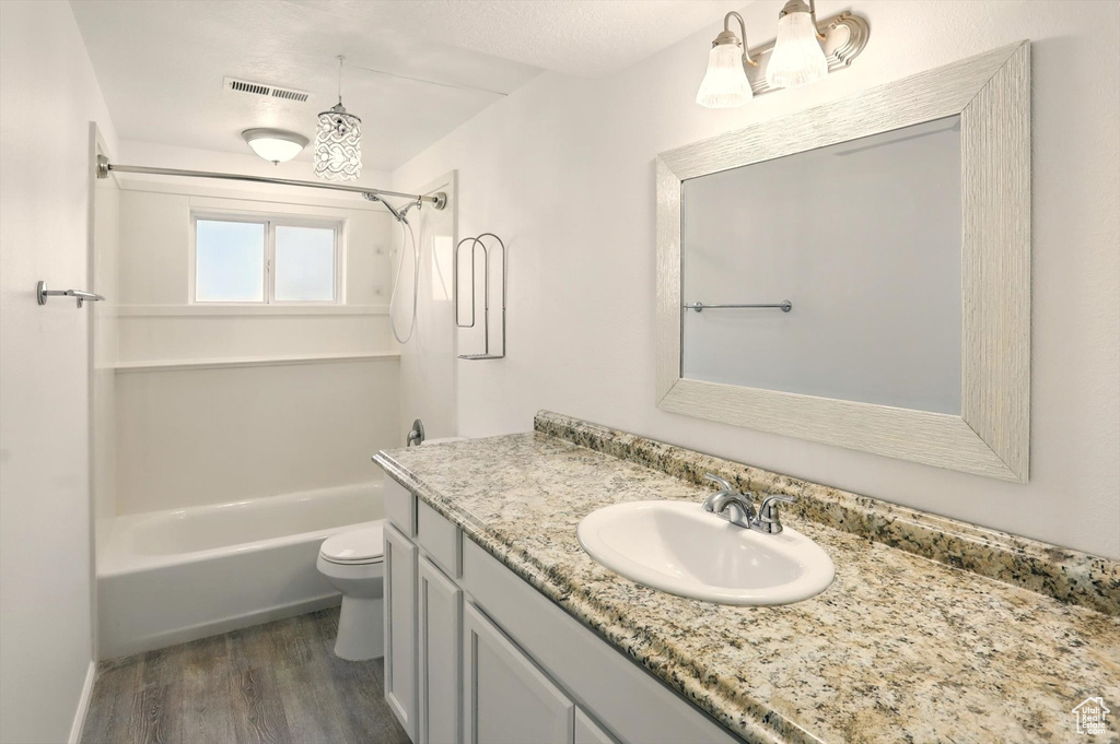 Full bathroom with visible vents, vanity, wood finished floors, toilet, and shower / tub combination