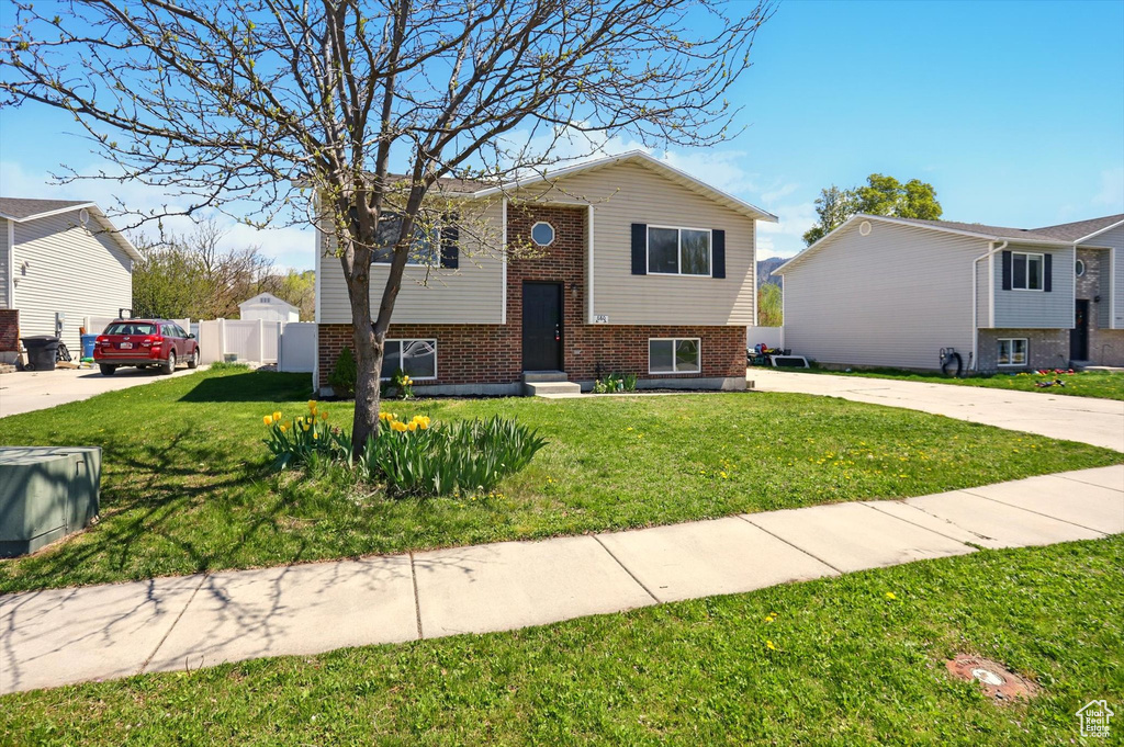 Bi-level home with fence, concrete driveway, a front lawn, and brick siding