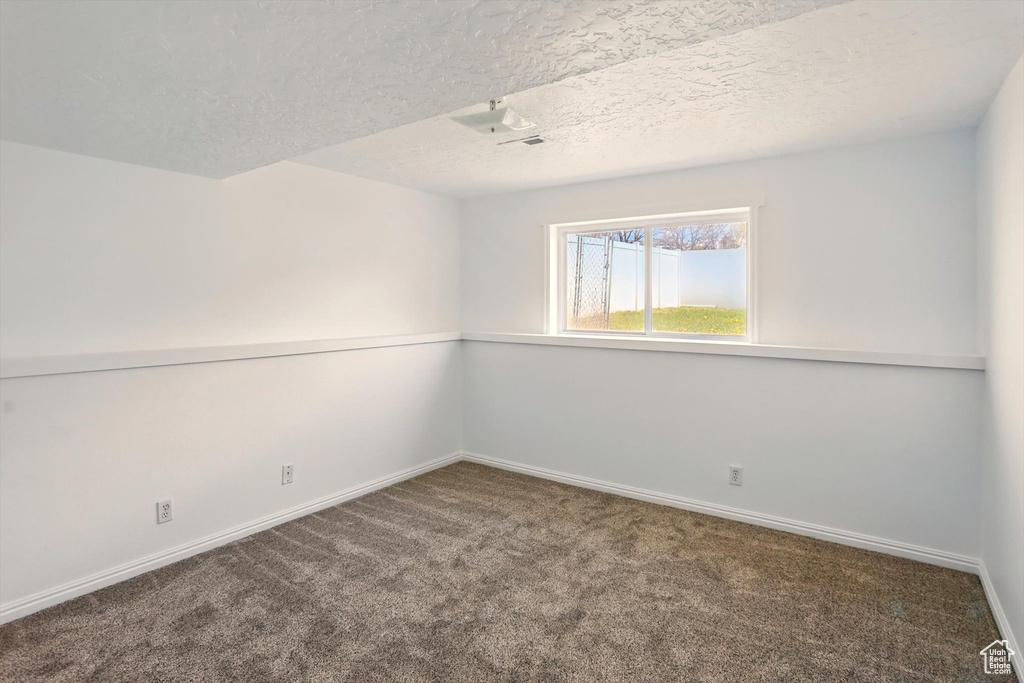 Empty room with baseboards, carpet, and a textured ceiling