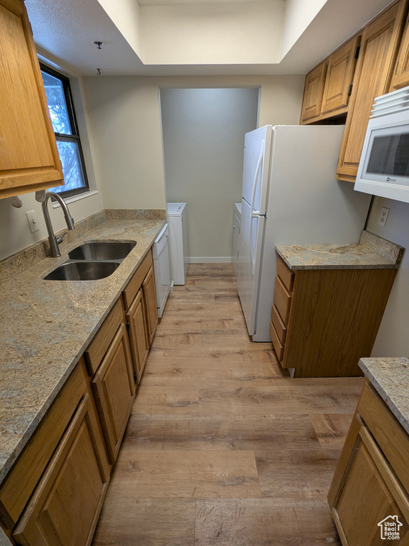 Kitchen featuring a sink, light stone counters, light wood-style floors, separate washer and dryer, and white appliances