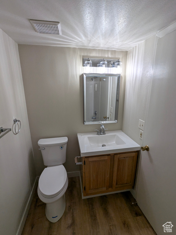 Bathroom with a textured ceiling, visible vents, wood finished floors, vanity, and toilet
