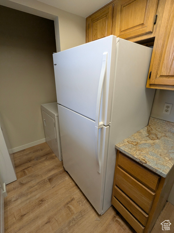 Kitchen featuring freestanding refrigerator, light wood-style floors, baseboards, brown cabinets, and light stone counters