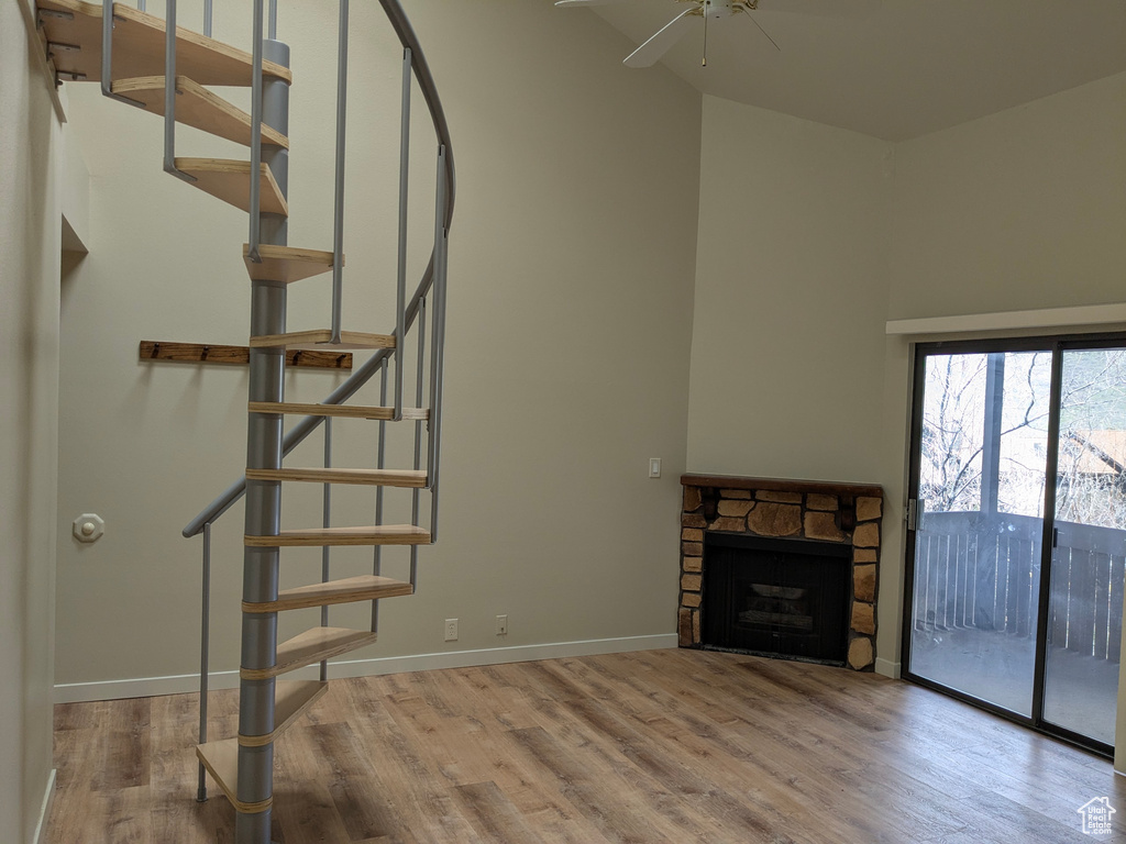 Unfurnished living room featuring wood finished floors, a stone fireplace, baseboards, stairway, and a ceiling fan
