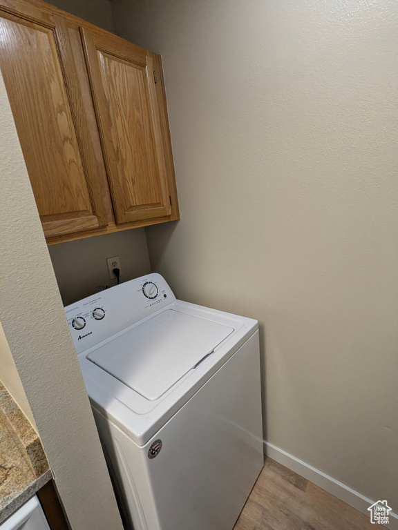 Laundry area featuring cabinet space, baseboards, washer / dryer, and light wood finished floors