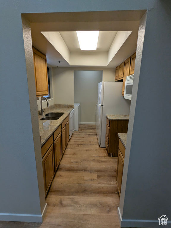 Kitchen featuring brown cabinets, a sink, a raised ceiling, white appliances, and light wood-style flooring
