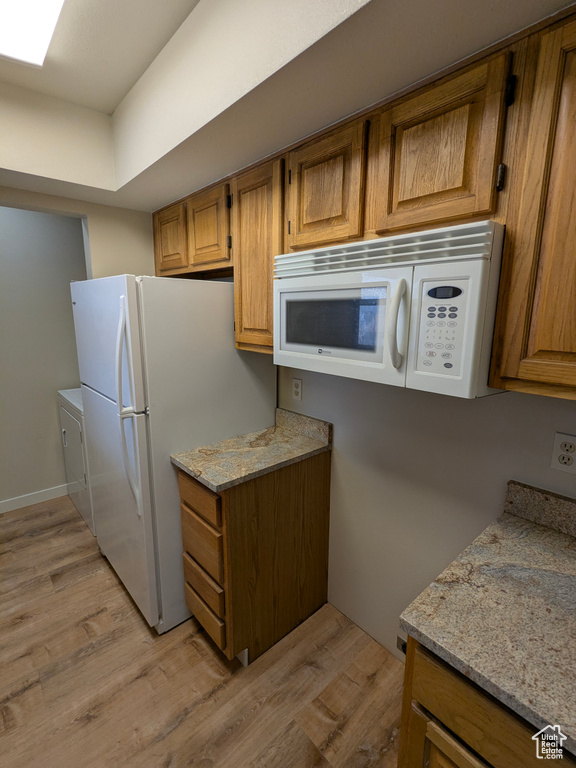 Kitchen with white appliances, brown cabinets, light stone counters, and light wood-type flooring