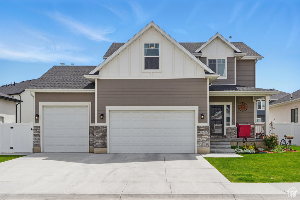 Craftsman-style house with an attached garage, stone siding, board and batten siding, a front yard, and concrete driveway