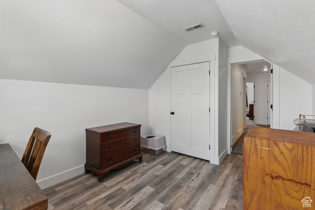 Office space with baseboards, vaulted ceiling, wood finished floors, and visible vents