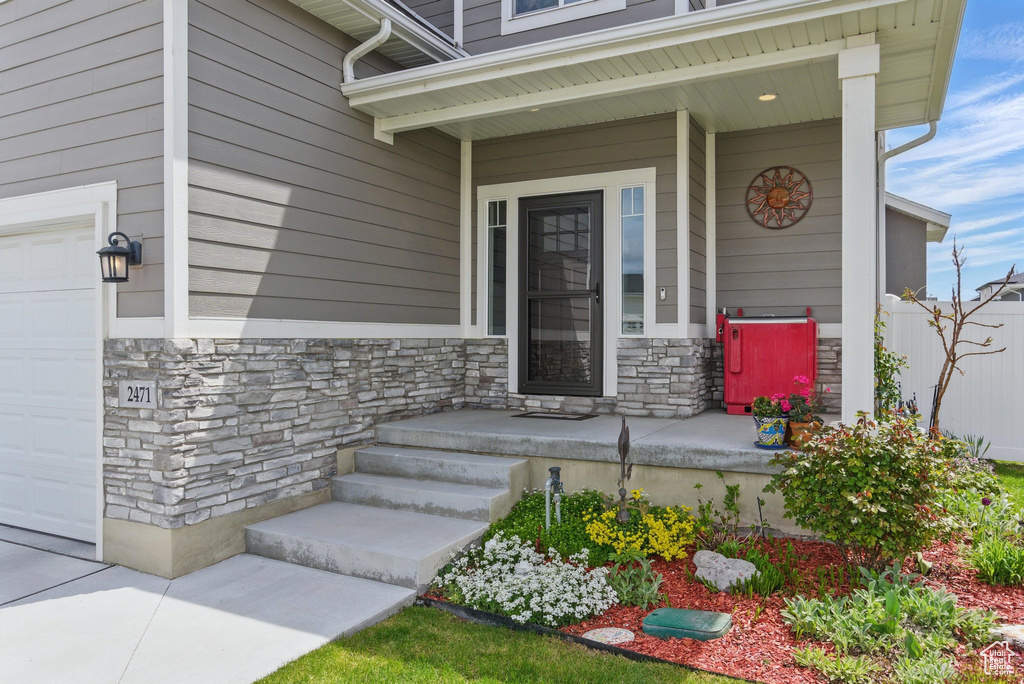 Property entrance with covered porch, an attached garage, and stone siding