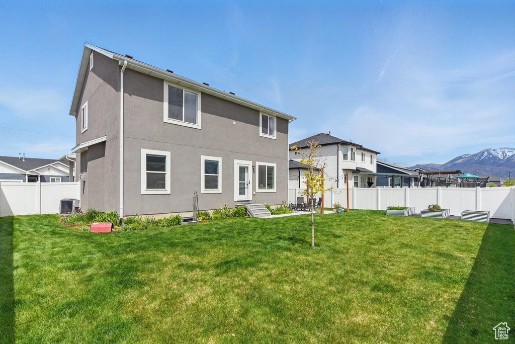 Back of house featuring cooling unit, a fenced backyard, stucco siding, a mountain view, and a yard