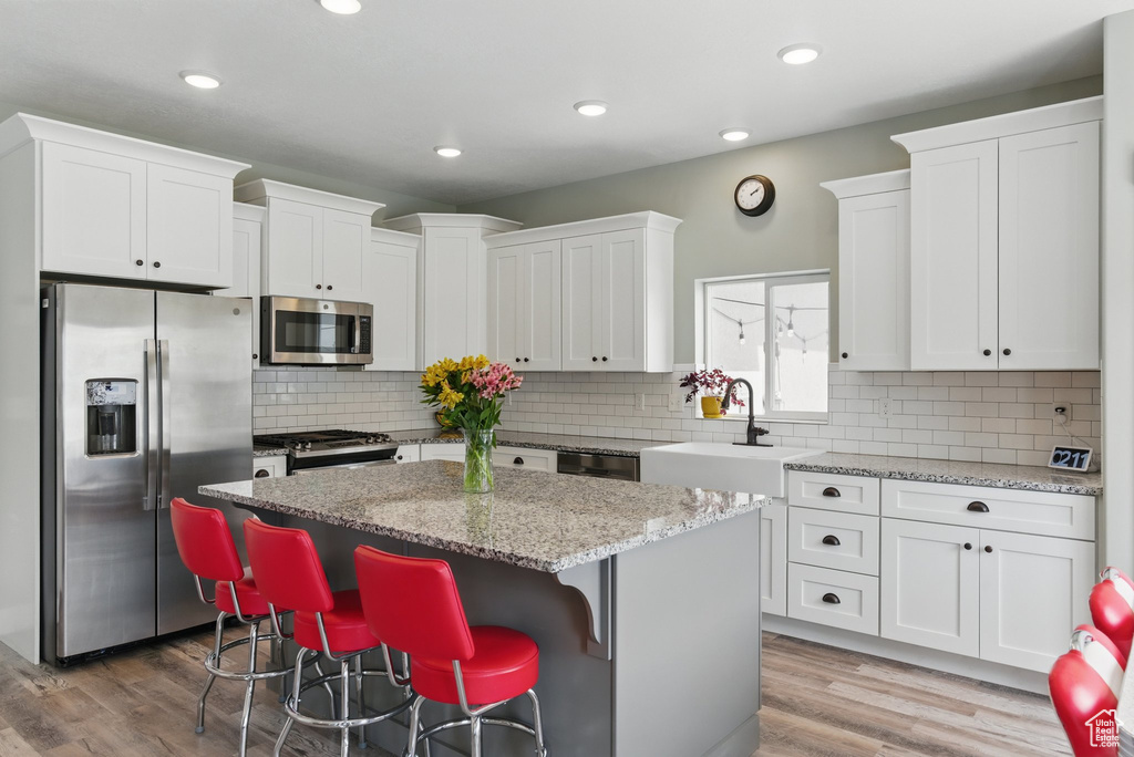 Kitchen featuring a sink, a center island, stainless steel appliances, white cabinetry, and decorative backsplash
