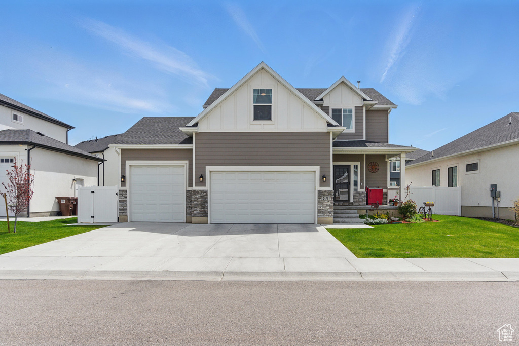Craftsman-style house featuring board and batten siding, a front yard, concrete driveway, an attached garage, and stone siding
