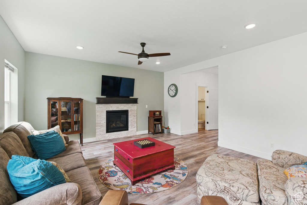 Living room featuring a ceiling fan, baseboards, wood finished floors, and a fireplace