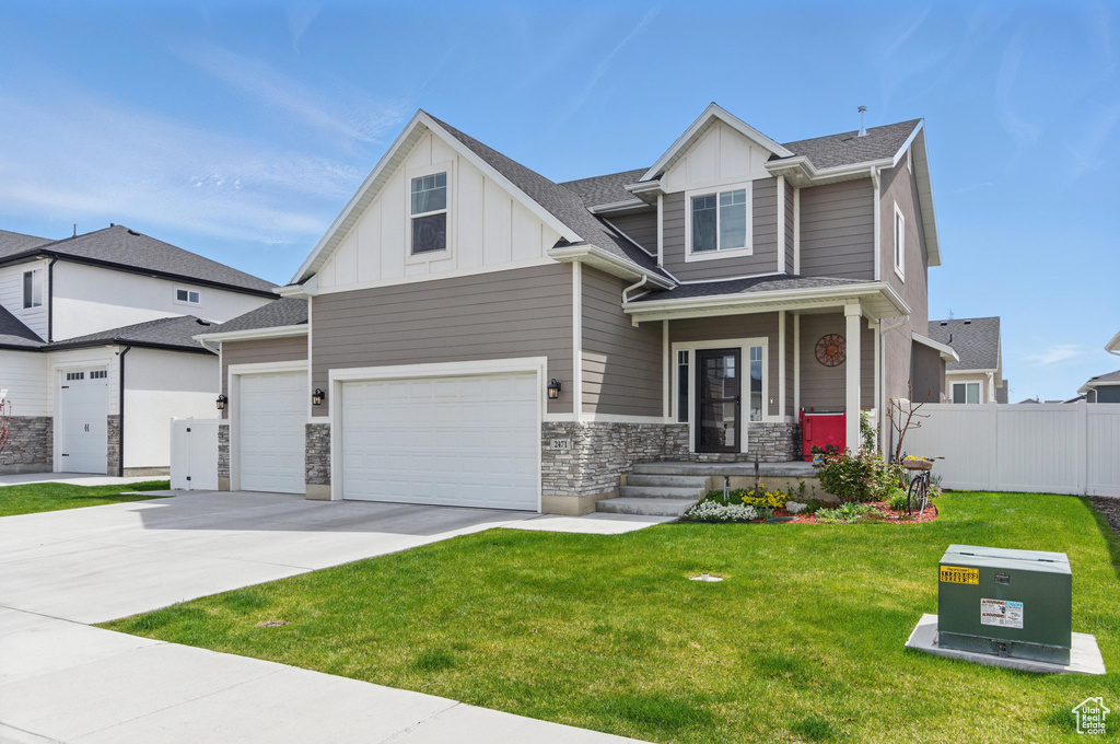 Craftsman-style home featuring fence, stone siding, a front yard, board and batten siding, and concrete driveway