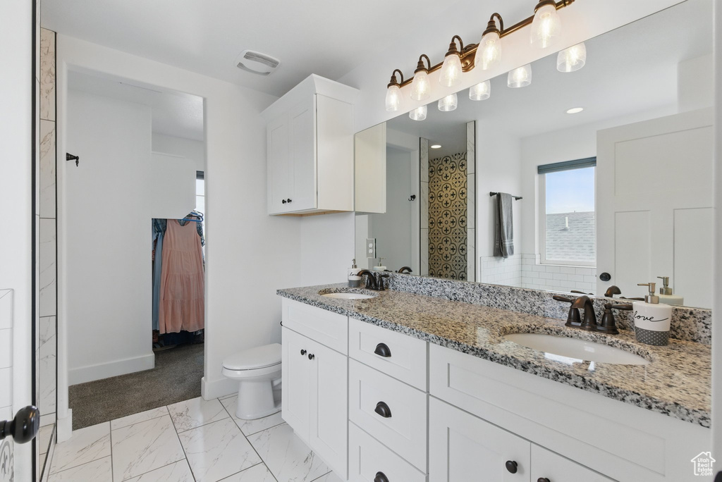 Full bath featuring double vanity, toilet, tiled shower, and a sink