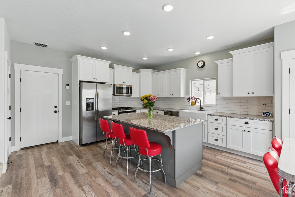 Kitchen featuring visible vents, appliances with stainless steel finishes, a center island, a sink, and white cabinetry