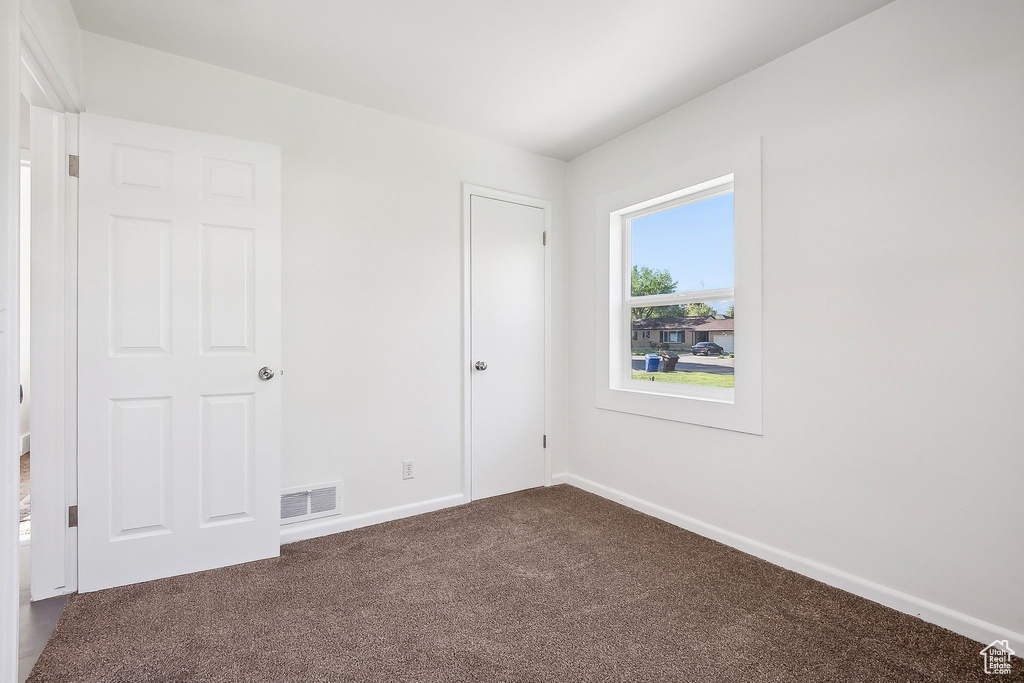 Unfurnished bedroom featuring visible vents, baseboards, and dark colored carpet