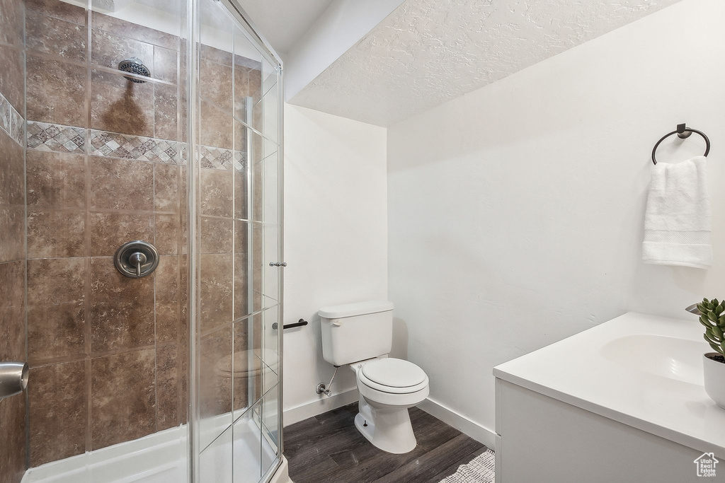 Full bathroom featuring vanity, toilet, baseboards, wood finished floors, and a stall shower