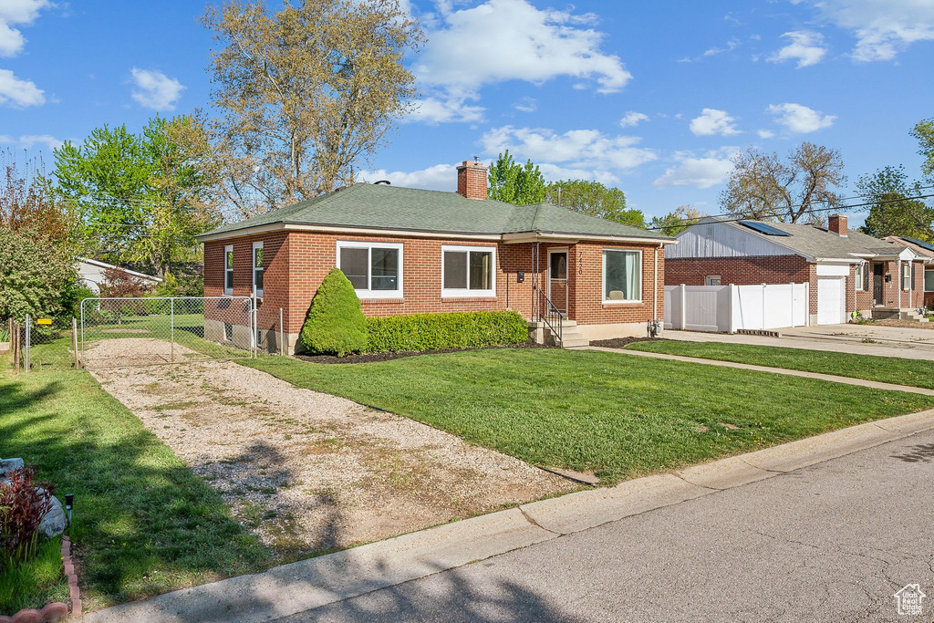 Bungalow-style home with a front lawn, fence, a chimney, brick siding, and concrete driveway