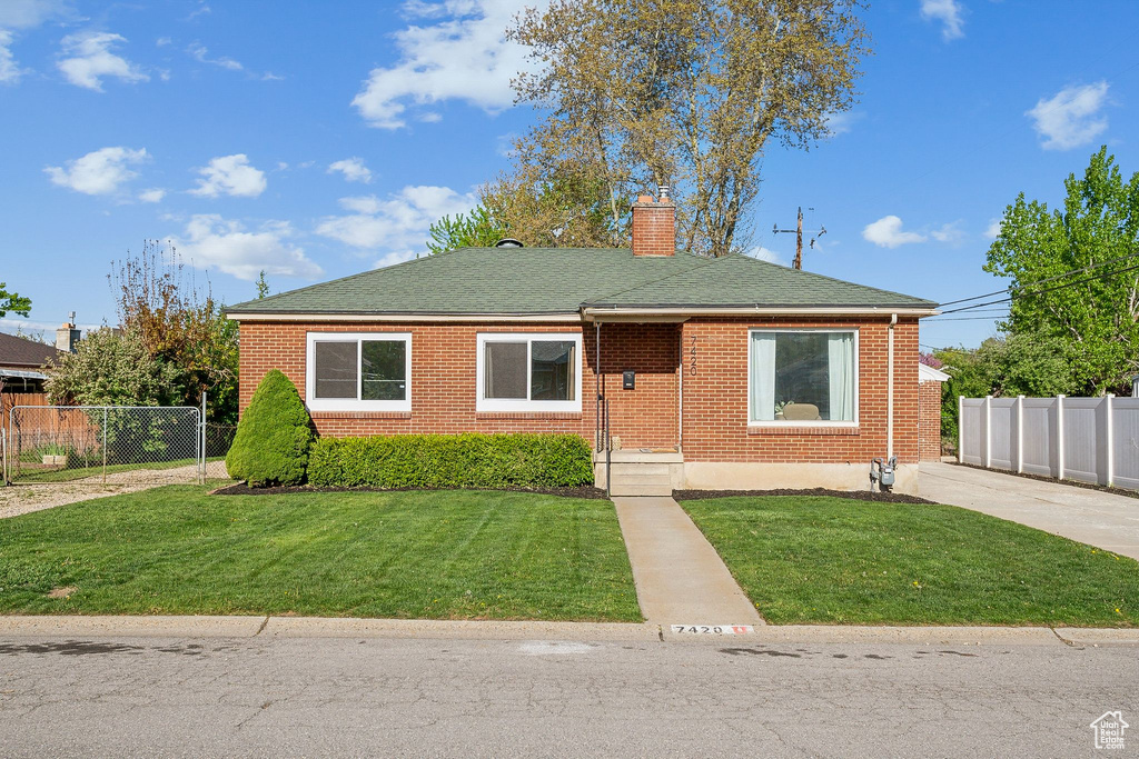 Bungalow-style home with a chimney, brick siding, fence, a front lawn, and a shingled roof
