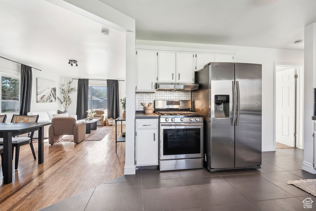 Kitchen featuring white cabinetry, under cabinet range hood, dark tile patterned flooring, tasteful backsplash, and stainless steel appliances