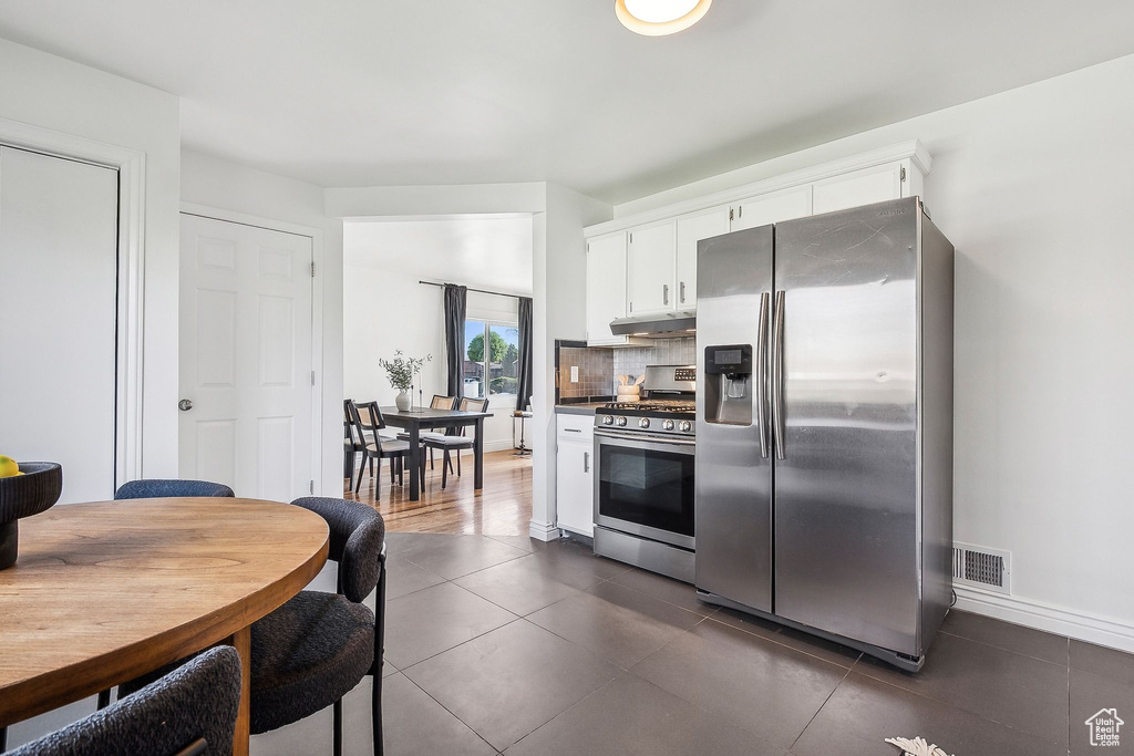 Kitchen featuring appliances with stainless steel finishes, white cabinetry, tasteful backsplash, under cabinet range hood, and dark tile patterned floors
