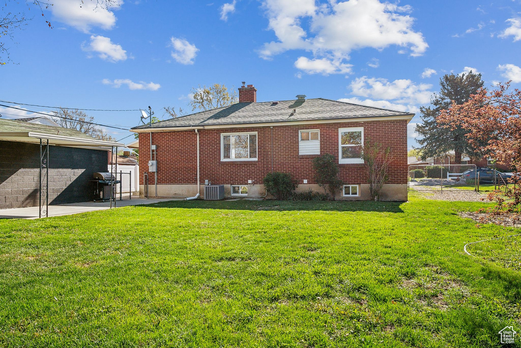 Rear view of house with fence, brick siding, central AC unit, a chimney, and a lawn