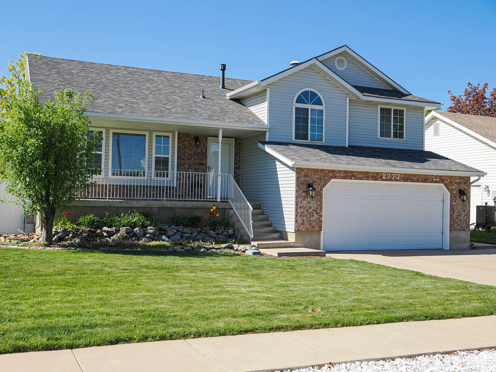 Split level home featuring concrete driveway, a porch, a front yard, and a garage