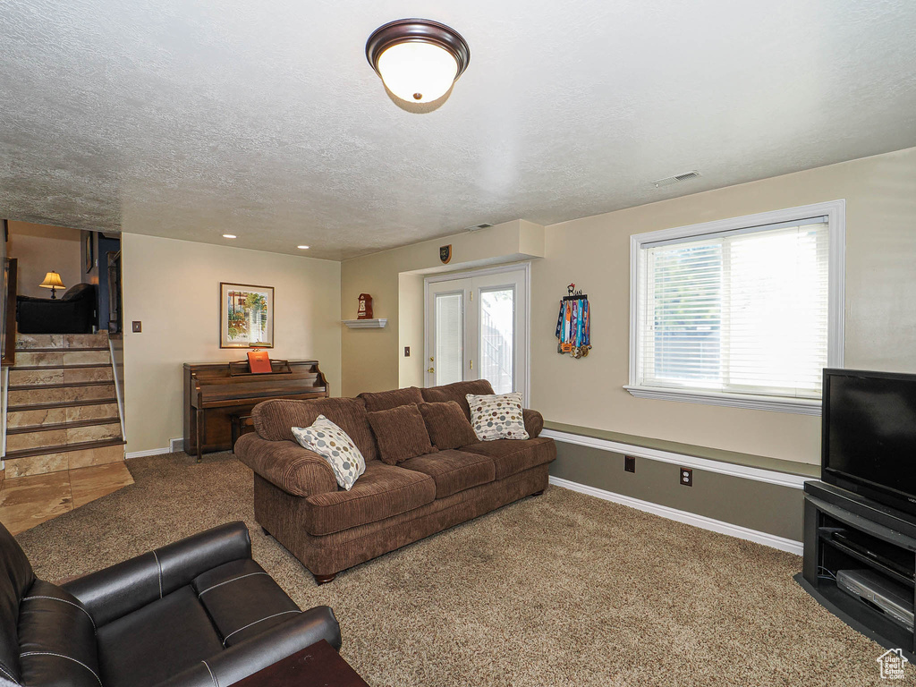 Carpeted living room featuring baseboards, a textured ceiling, stairs, and visible vents