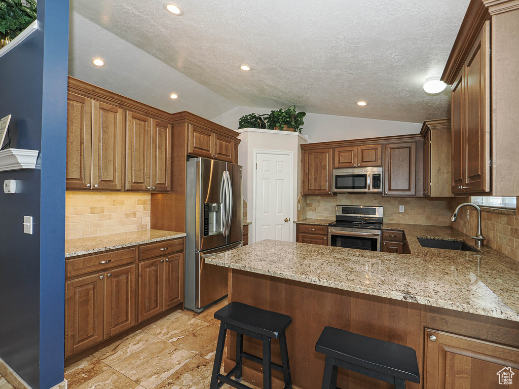 Kitchen with a peninsula, lofted ceiling, light stone countertops, a sink, and stainless steel appliances