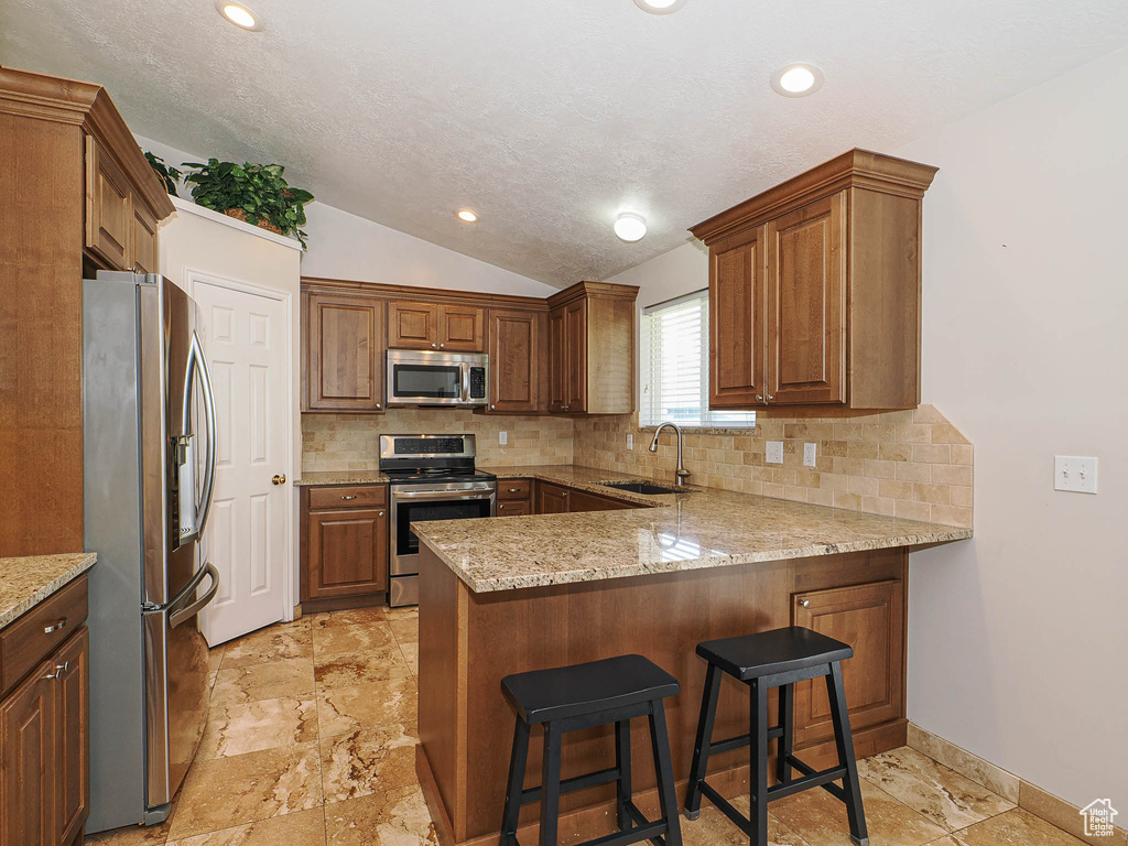 Kitchen with a sink, decorative backsplash, a peninsula, and stainless steel appliances