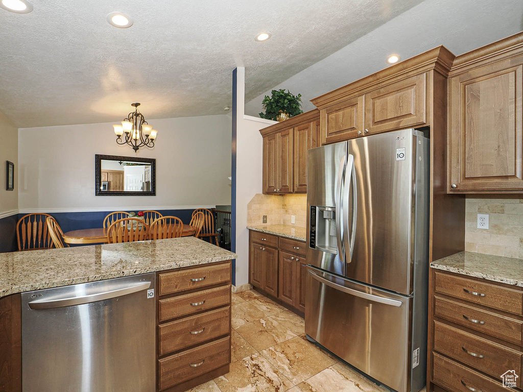 Kitchen featuring brown cabinets, stainless steel appliances, a notable chandelier, and backsplash