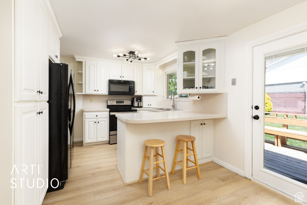 Kitchen with a sink, black appliances, light wood finished floors, a peninsula, and glass insert cabinets