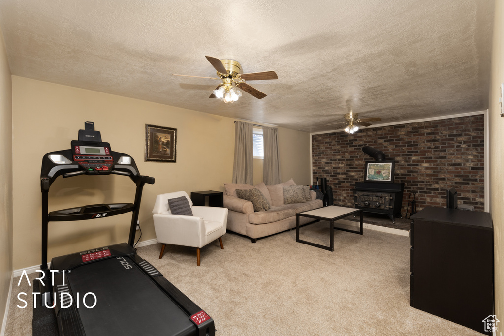 Workout room featuring a wood stove, carpet floors, a textured ceiling, a ceiling fan, and baseboards