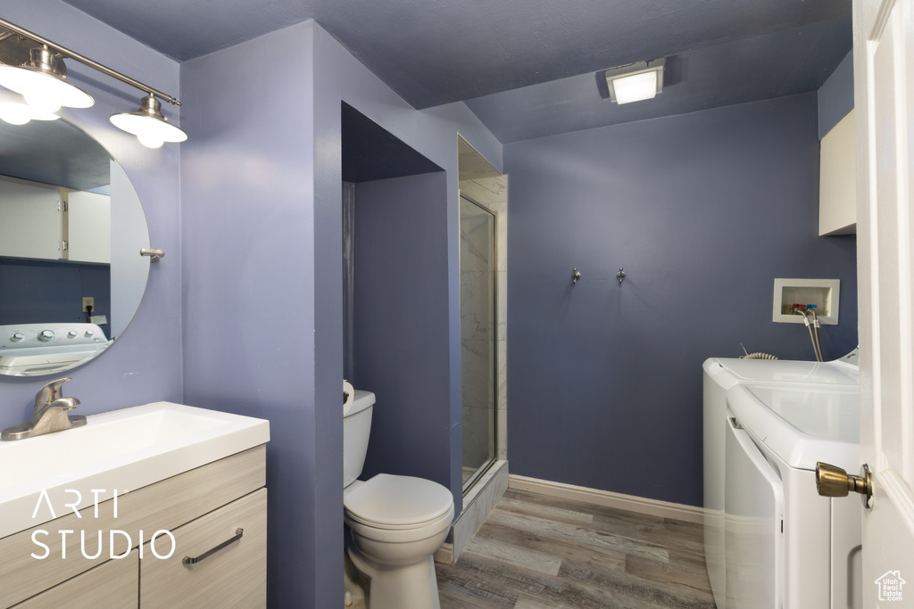 Full bathroom featuring vanity, wood finished floors, washer and dryer, toilet, and a shower stall