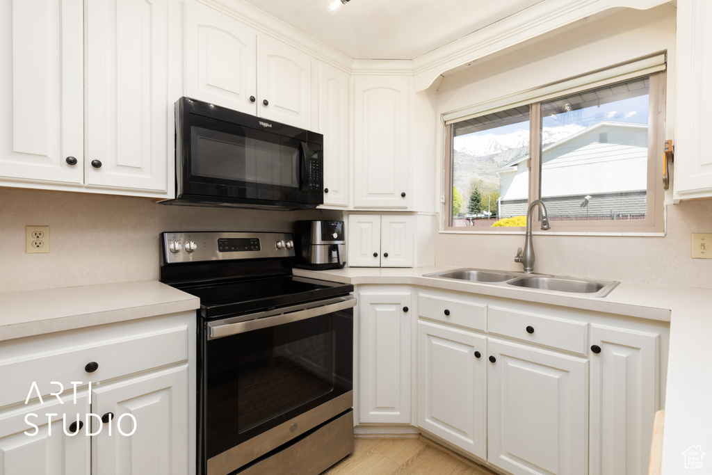 Kitchen with black microwave, stainless steel range with electric cooktop, light countertops, a sink, and white cabinetry