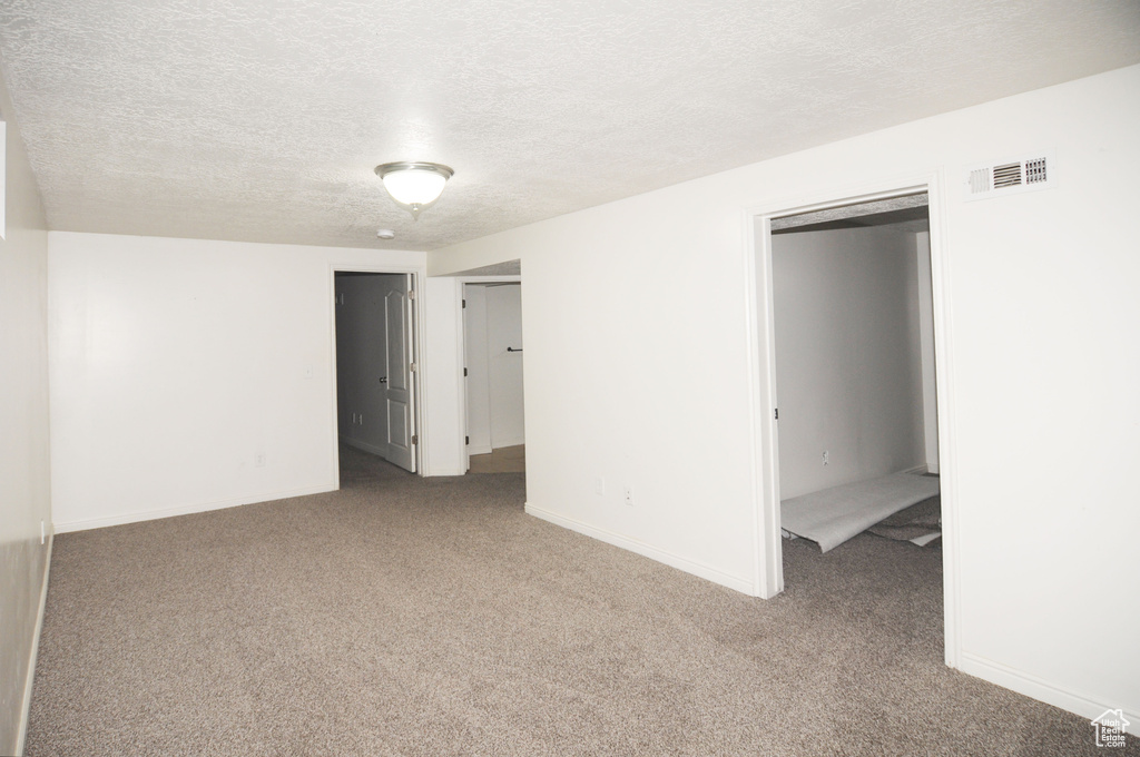 Unfurnished bedroom featuring a textured ceiling, visible vents, baseboards, and carpet floors