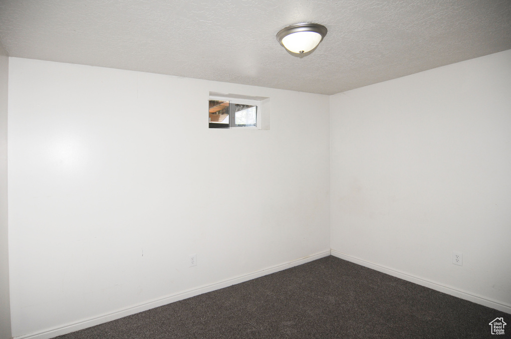 Below grade area featuring dark carpet, a textured ceiling, and baseboards