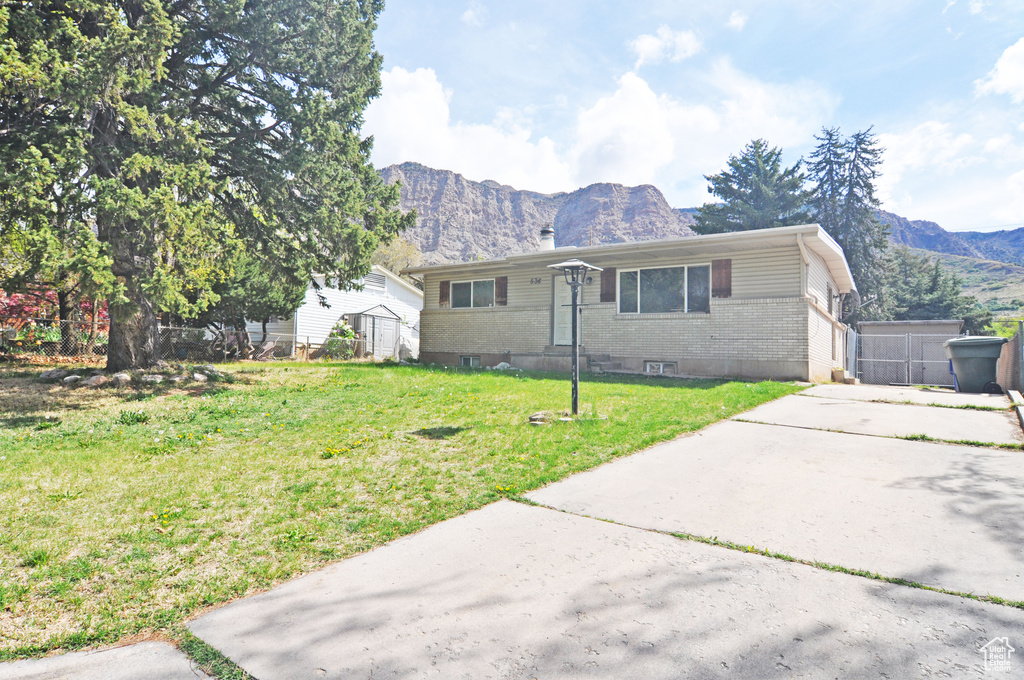 View of front of house featuring a front lawn, a mountain view, brick siding, and an outbuilding